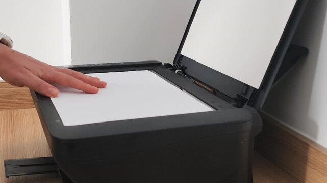 Process of copying paper documents in business office. Human hand places white sheet on scanner glass to safely clone and archive corporate paper documents for modern digital management.
