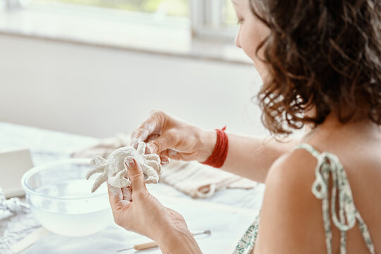 Focused young woman modeling small clay sculpture at table in her art studio. Creative hobby and handmade pottery concept.