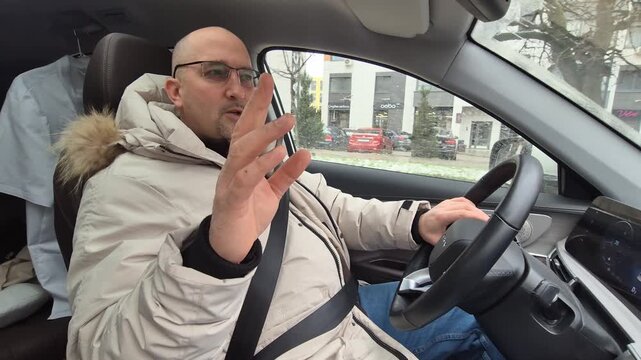 Professional driver talks while operating a vehicle on city streets, showing directions with hand gestures. Medium shot from the passenger seat.