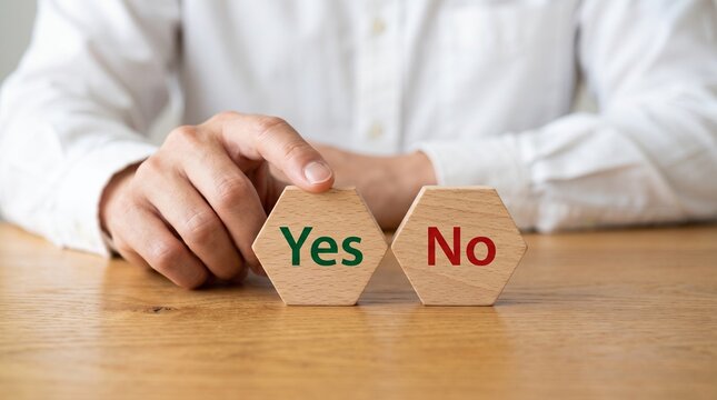 A person in a white shirt touches a hexagonal wooden block with the word yes printed in green next to another block labeled with no