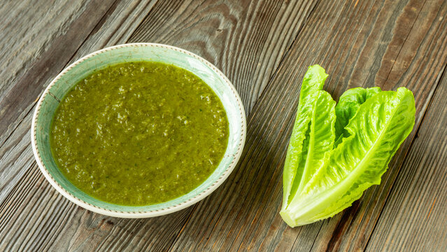 French romaine lettuce soup with mint in bowl on rustic wooden background with fresh lettuce heart on the side
