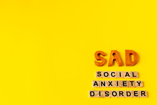 Social anxiety disorder and SAD abbreviation spelled with wooden blocks in the bottom right corner on a yellow background with large copy space.