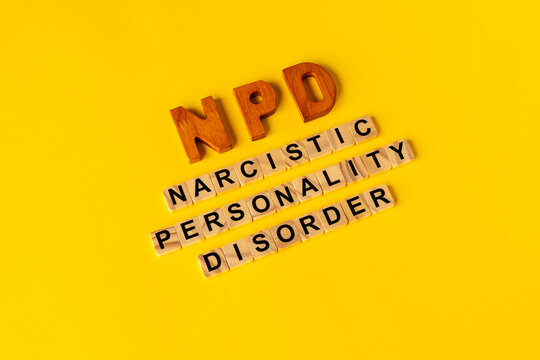 Diagonal typography layout of the NPD abbreviation and Narcissistic Personality Disorder words spelled with wooden letter tiles on a vibrant yellow background.