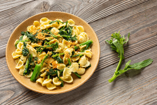 Traditional Italian orecchiette con cime di rapa pasta with crunchy muddica topping and raw broccoli rabe sprig with bud on the side