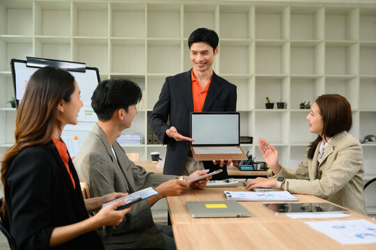 Asian Business Leader Presenting Laptop Screen to Team During Strategic Office Meeting