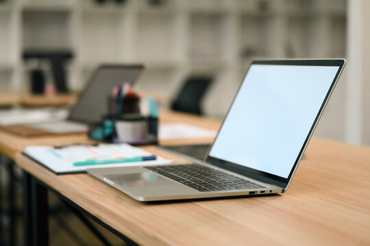 Laptop with Empty White Screen on Wooden Desk in Modern Office or Classroom Setting