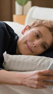 Happy Caucasian woman lying in bed at morning checking mobile phone gadget addicted female using smartphone check messages relaxing in bedroom smiling girl relax reading notification smile at home