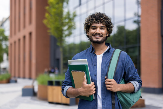 Young indian student standing on a modern university campus, carrying books and a backpack, reflecting academic pursuits and positive learning experiences