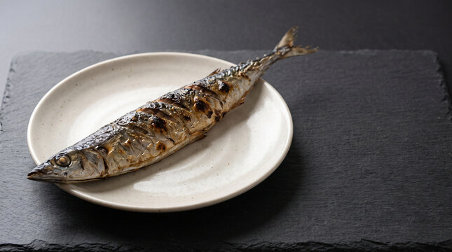 Traditional Japanese grilled pacific saury sanma served on long ceramic plate on dark table