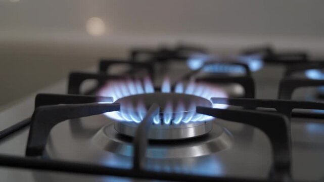 Close up of a blue burning flame on a modern stainless steel kitchen gas stove burner for cooking food and home meal preparation