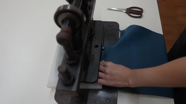 Worker feeds blue leather sheet into manual die cutting press