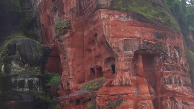 A low-angle tracking shot panning from the surrounding red sandstone grottoes up to a close-up of the serene face and detailed head of the Giant Buddha.