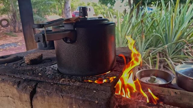 Slow-motion close-up, pressure cooker heating over a wood fire on a rustic outdoor stove, showing traditional cooking and off-grid food preparation