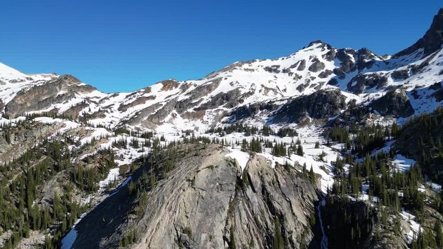 4k drone shot of Gwillim Lake in Valhalla Provincial Park with melting snow in june and rocks in the foreground.