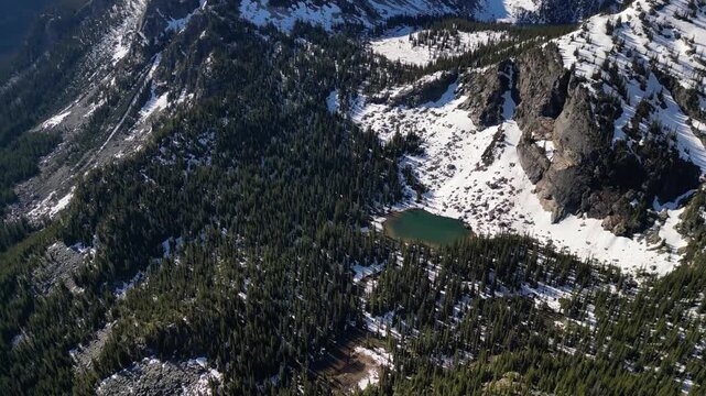 Drone shot of a mountain lake in Bristish Columbia with pine tree, melting snow in Valhalla Provincial Park,