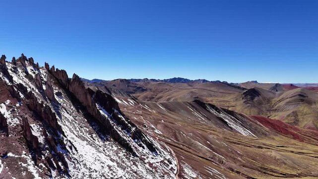 An aerial view of the rugged snow-dusted stone forest formations at Palccoyo Rainbow Mountain under a clear blue sky in the Peruvian Andes