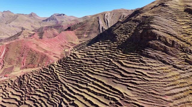 Aerial drone view of ancient agricultural stone terraces carved into the steep slopes of the high Peruvian Andes under a clear blue sky