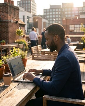 Businessman working on laptop at rooftop coworking terrace during sunset. Concept of remote business, flexible workspaces, entrepreneurship and digital productivity.