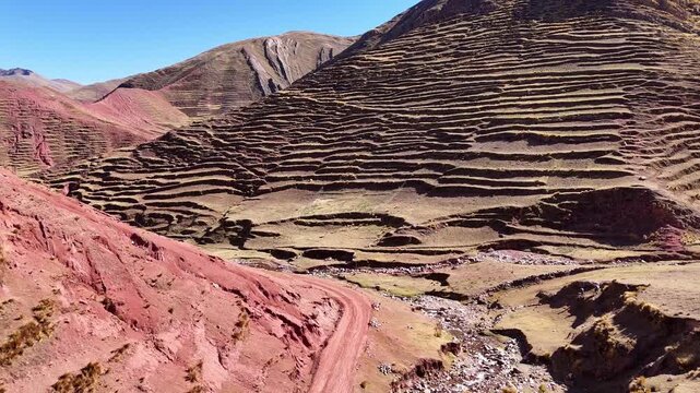 Aerial drone view of a small river flowing through a mountain valley with ancient agricultural terraces on steep slopes in the Peruvian Andes