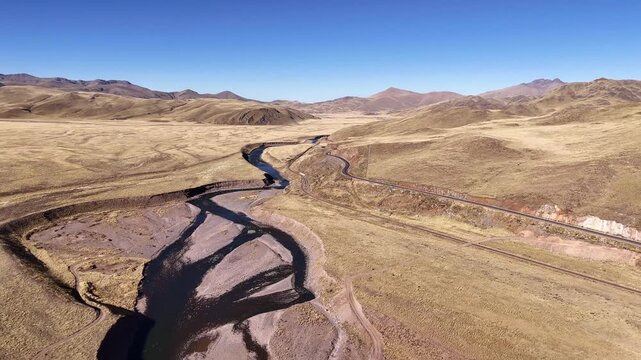 Aerial view panning from right to left across the meandering Rio Ramis, a road, and railway line cutting through the vast Peruvian altiplano
