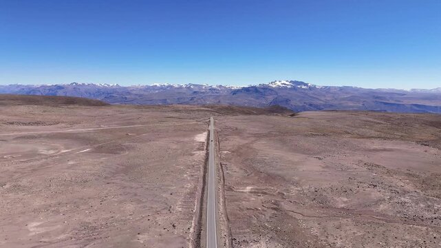 Aerial view of a car driving down the long straight highway 1S towards the snow-capped Mount Mismi in the high Andes plateau near Chivay, Peru