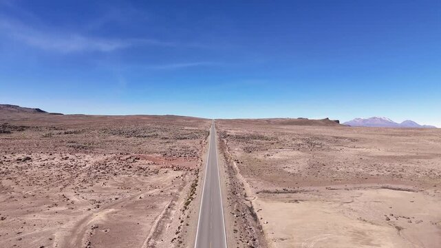 Aerial view of a car driving on a long straight asphalt highway stretching across the vast arid Altiplano plains toward El Misti volcano in Arequipa, Peru