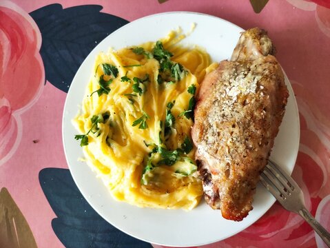 Roasted chicken leg with mashed potatoes and fresh parsley on a white plate