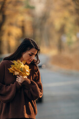 Naklejka premium Fallen leaves in hands. A woman is standing on the asphalt road outdoors at autumn season
