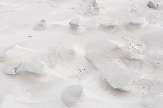 Wind-sculpted sand mounds are forming ripples on dune close-up, showing pebbles and shell fragments