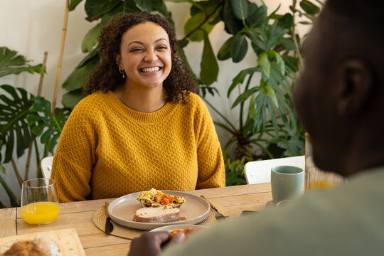 African American couple sitting at home table, woman laughing wearing mustard sweater with eggs