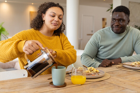 Couple having breakfast at home, woman pouring coffee from French press into green mug