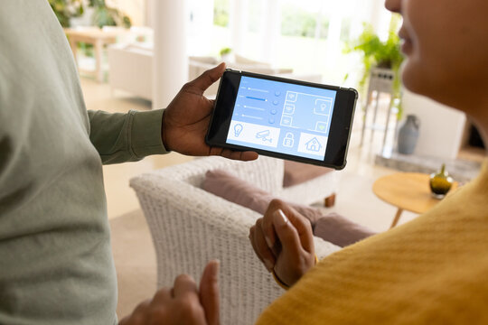 Tablet is displaying smart-home control interface in bright living room, with woven chair and plant