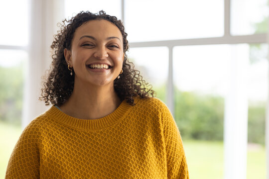 African American woman smiling near multi-pane windows, wearing mustard knit and gold hoops