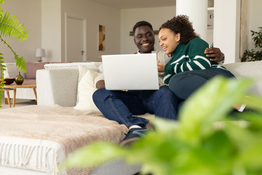 African American couple sitting on sectional sofa leaning over silver laptop woman in green sweater