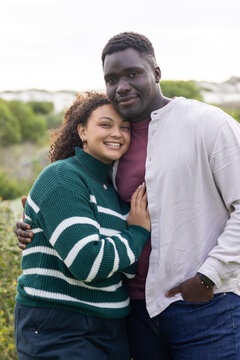 African American couple standing close on dunes, leaning, smiling, wearing green sweater and watch