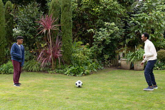 African adolescent and adult males standing facing each other on backyard lawn with soccer ball