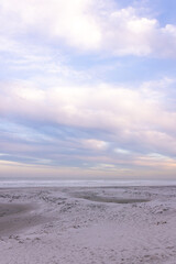 Obraz premium Sandy shoreline revealing shallow tidal pools and scattered seaweed at low tide, pastel sky glowing