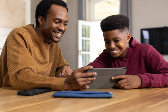 Father and teenage son brown sweatshirt, maroon hoodie leaning at tablet at home with blue pouch