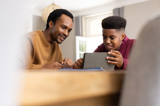 African American father and teenage son watching tablet with cover at wooden table at home