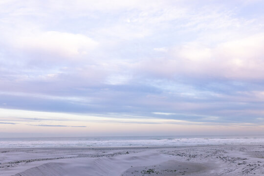 Sandy beach and low dunes are glowing under pastel clouds with gentle surf and wet sand