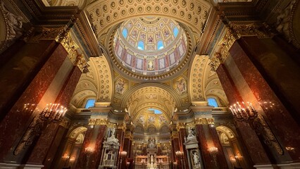 Grand interior of St. Stephen's Basilica in Budapest with ornate gilded dome ceiling, marble columns and glowing candlelit altar viewed from below © GIHUN KIM