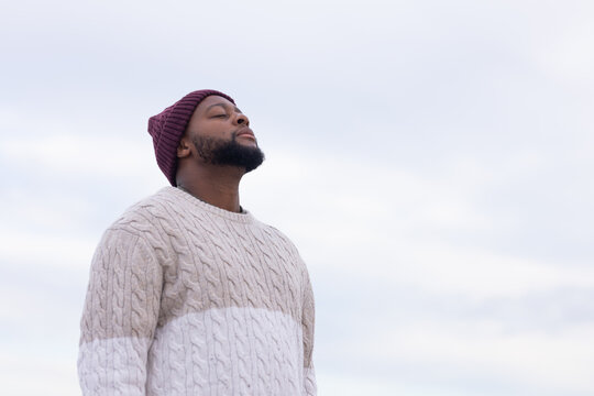 African American man standing outside looking up wearing knit sweater maroon beanie, copy space