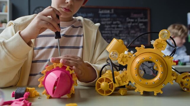 Caucasian child using screwdriver, assembling plastic robot toy during STEM class. Footage is ideal for educational marketing, STEM school promotions, and technology learning advertisements