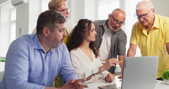 Adults students with instructor during laptop training. The team in a meeting for discussion and teamwork, practicing learning on a laptop in a workshop. Clear concept of adult group training.