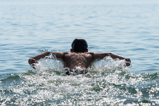 Young competitive swimmer performing butterfly stroke during open water training in sea. Rear view of an male athlete demonstrating endurance, strength and professional swimming technique
