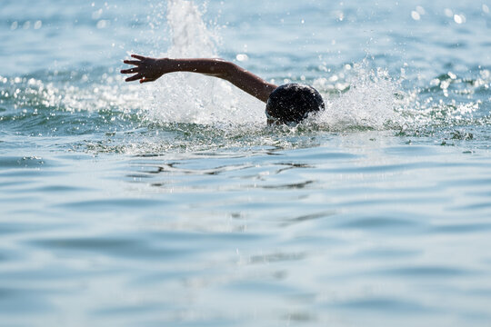 Teenage swimmer practicing freestyle crawl stroke in open ocean water during endurance training. Dynamic outdoor sports scene with young professional triathlon swimmer, splashing water and copy space