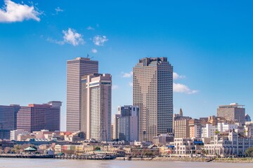 Obraz premium New Orleans skyline rises above the waterfront on a sunny day, framed by modern towers and a clear blue sky.
