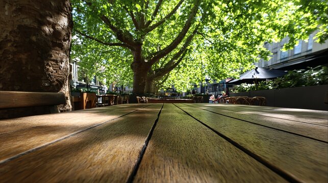 Sunlight filters through lush green leaves, illuminating a wooden patio table in a vibrant urban park setting, creating a peaceful atmosphere