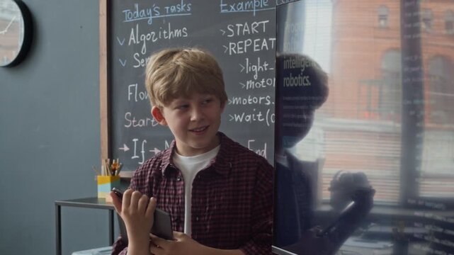 Caucasian boy holding tablet, explaining robotics programming code on interactive screen in classroom. Clip is suitable for promoting STEM education and modern school curricula