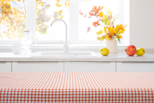 Empty checkered tablecloth on a kitchen table with autumn decor and fruit in the blurred background